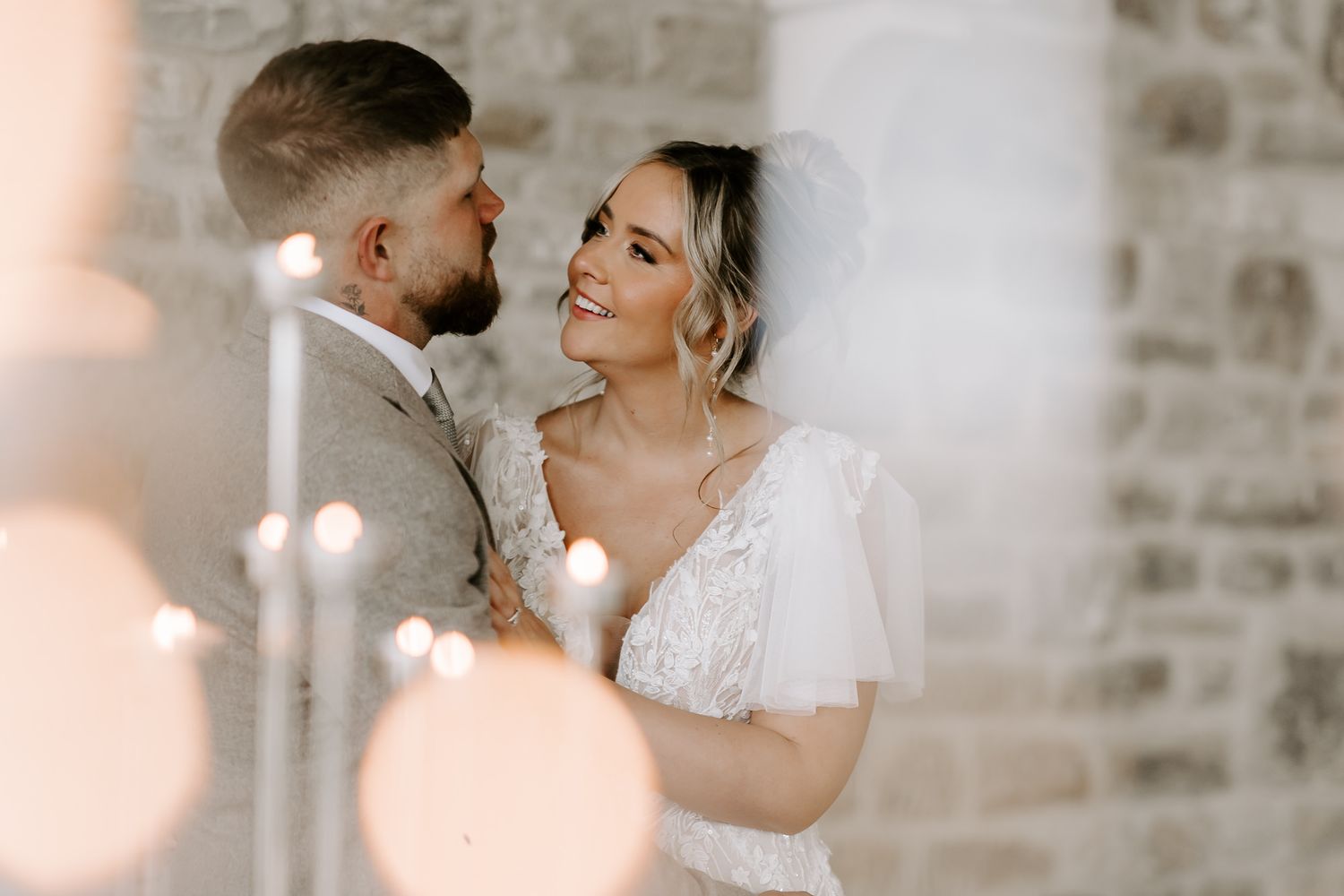 A wedding couple shares a romantic moment in front of a rustic stone wall with soft lighting.