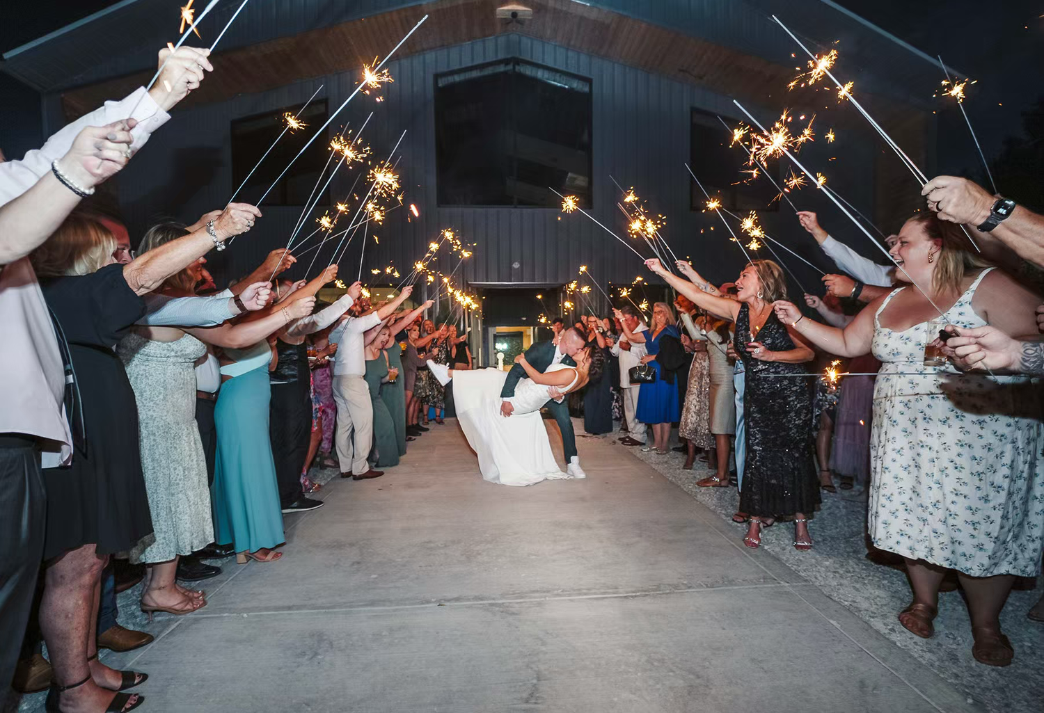 Wedding guests hold sparklers in a line formation creating a magical walkway tunnel during an evening celebration.