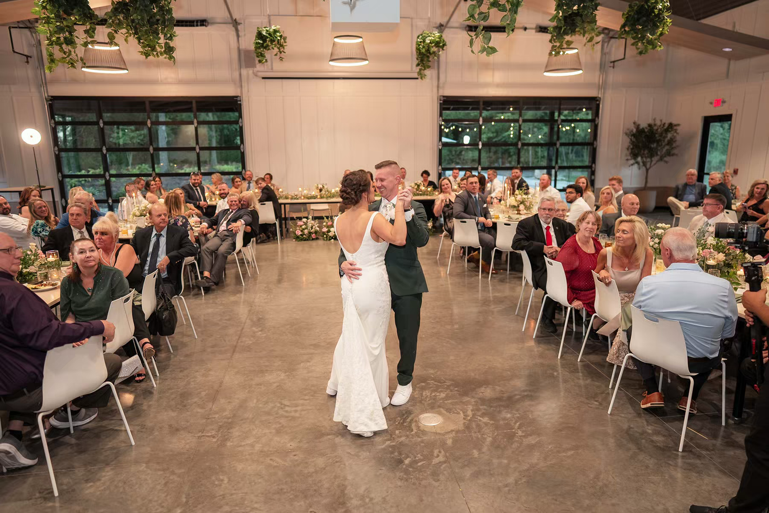 A wedding reception venue with round tables and chairs set up in a large indoor space with green accents and lighting.