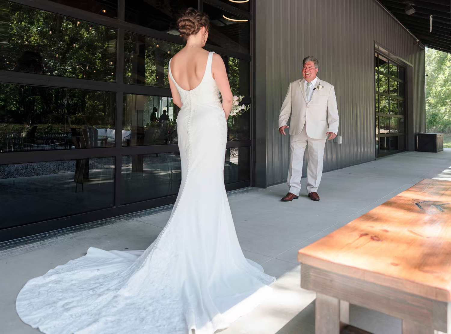 A bride in a flowing white wedding dress with a long train walks down a covered outdoor walkway.