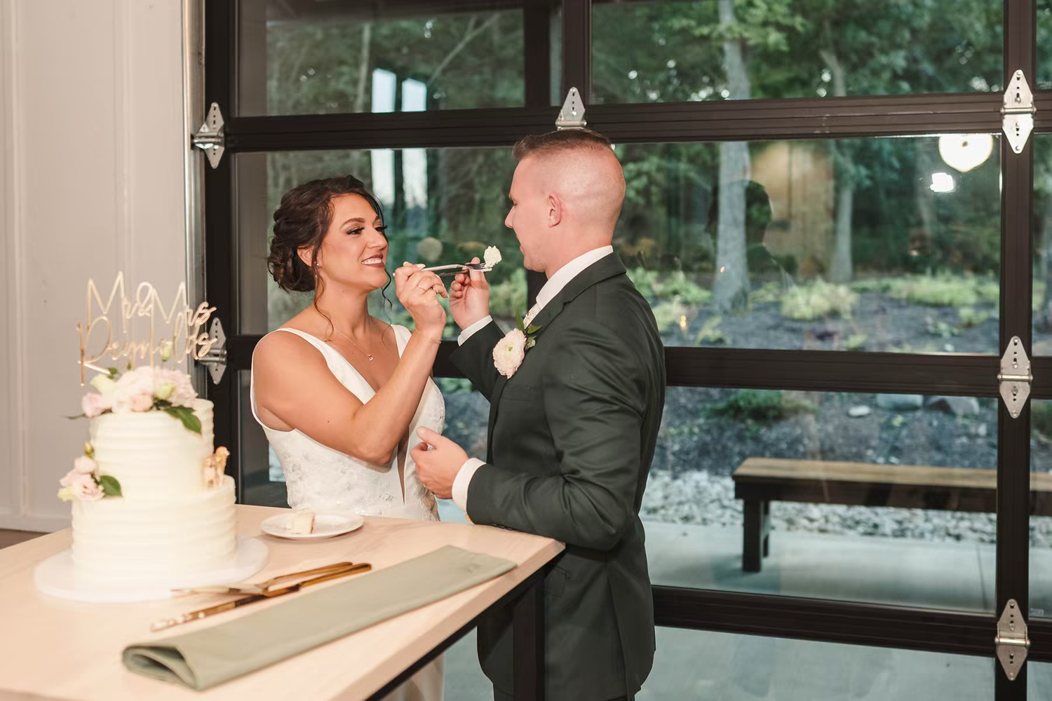 A bride and groom share an intimate moment during their wedding reception in front of large windows.