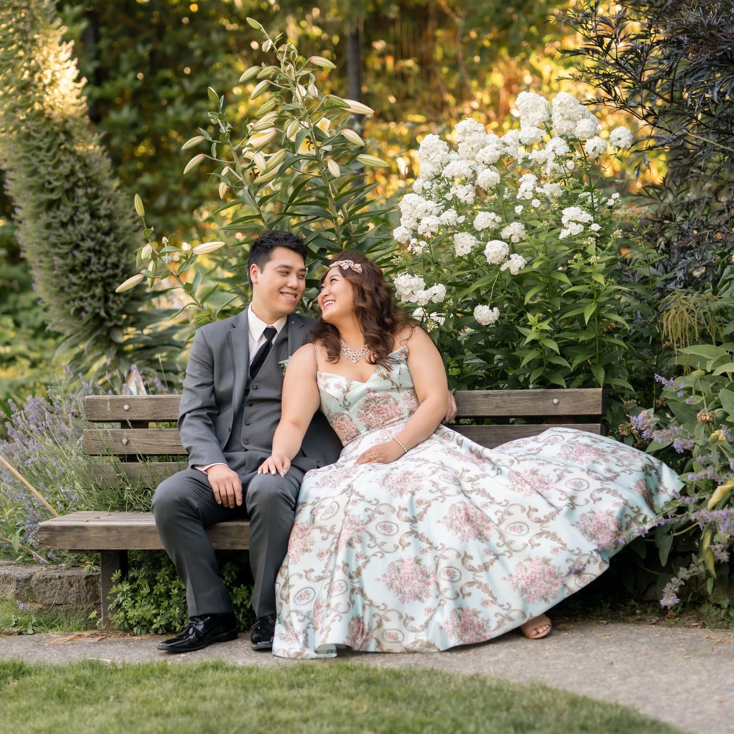 Romantic garden scene with couple sitting on bench surrounded by blooming flowers and greenery at Tacoma Rose Garden by Filling the Frame.