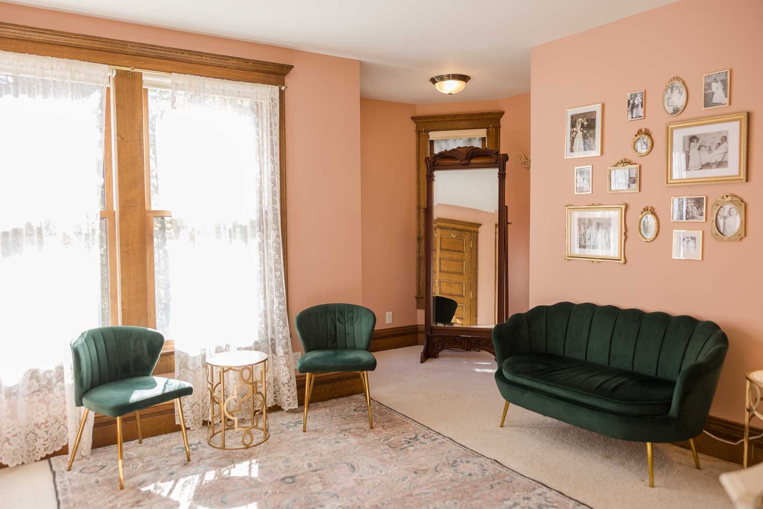 Vintage living room with emerald green velvet sofa and chairs against salmon pink walls adorned with framed photos.