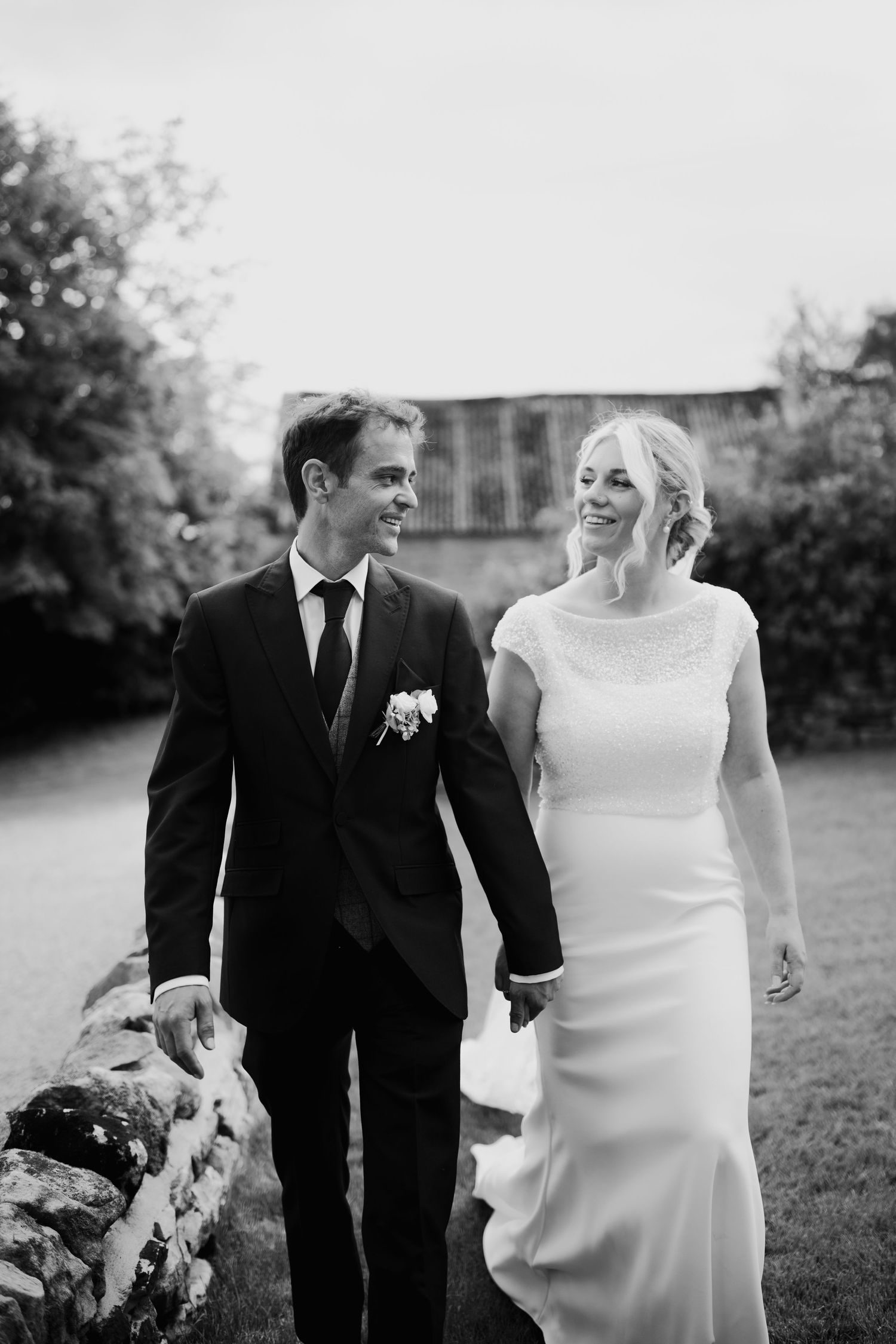 A romantic black and white photo series of newlyweds walking together outdoors in formal wedding attire.
