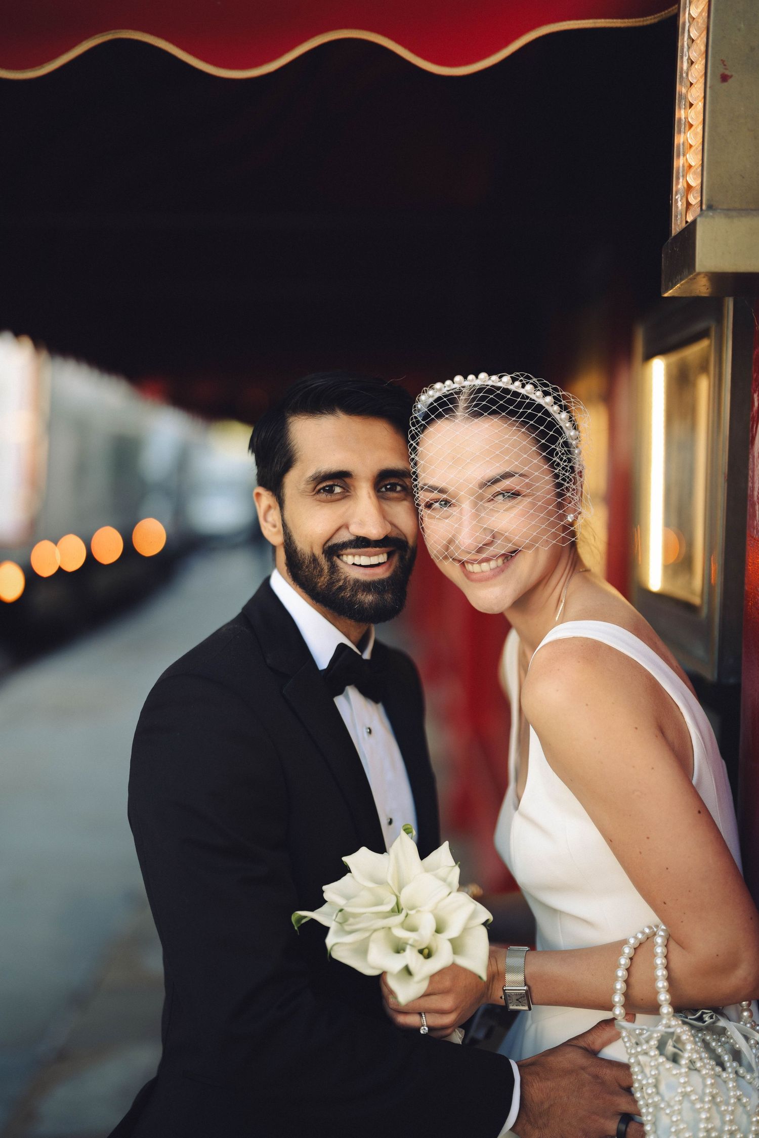Elegant evening wedding portrait with red velvet backdrop and white floral bouquet.