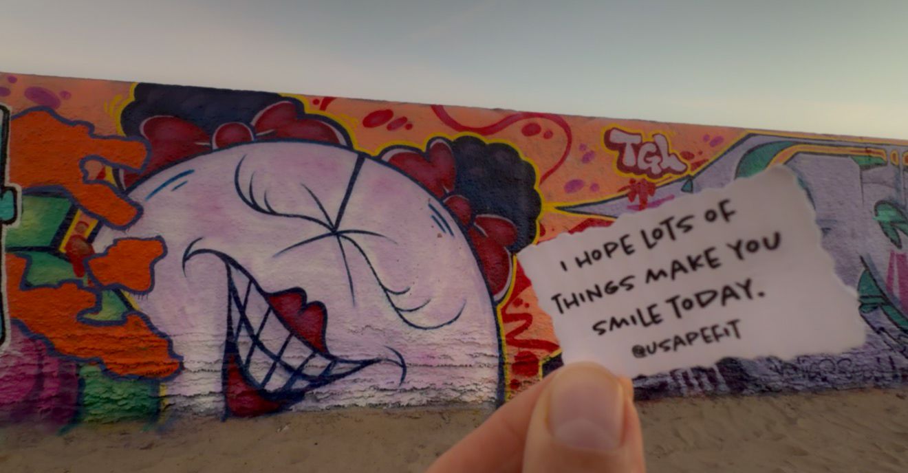 Colorful street art mural featuring a large smiling face design and text against a wall.