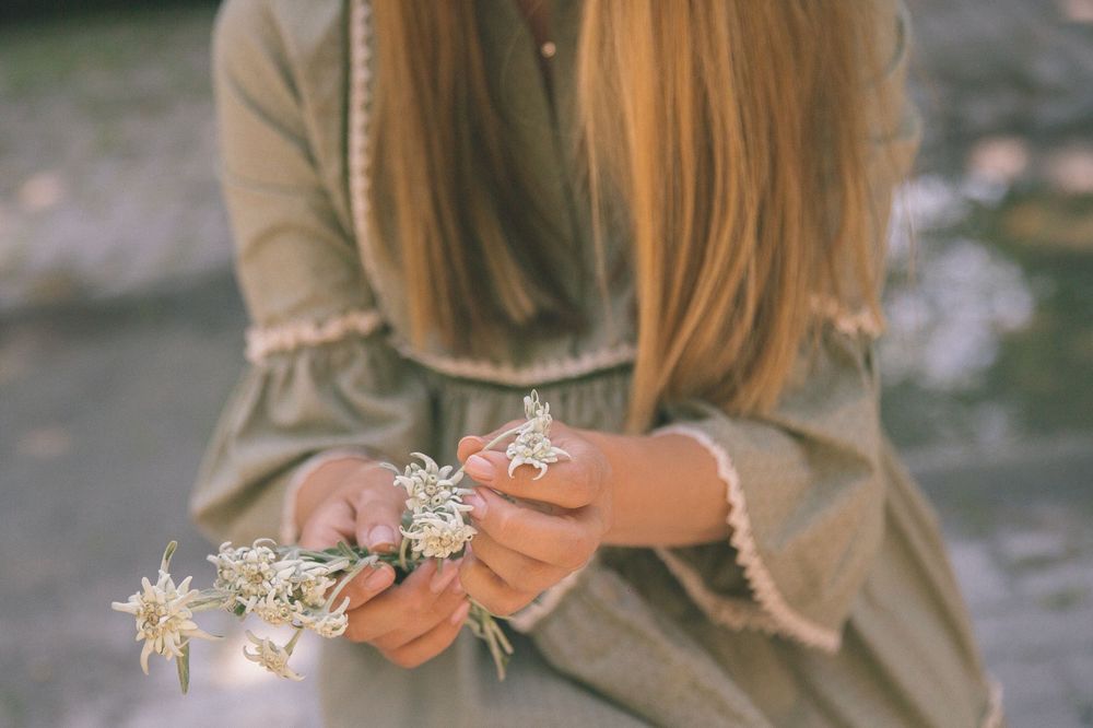 A person in a tan sweater holds delicate dried white flowers against a blurred outdoor background.