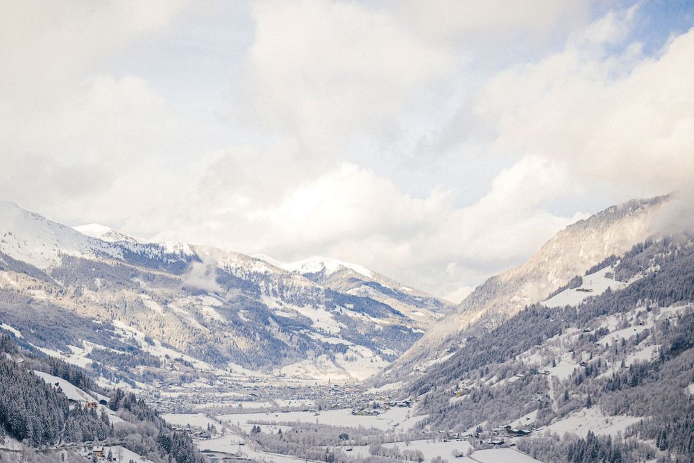 A panoramic winter view of snow-covered mountains and valleys with low-hanging clouds in the Alps.