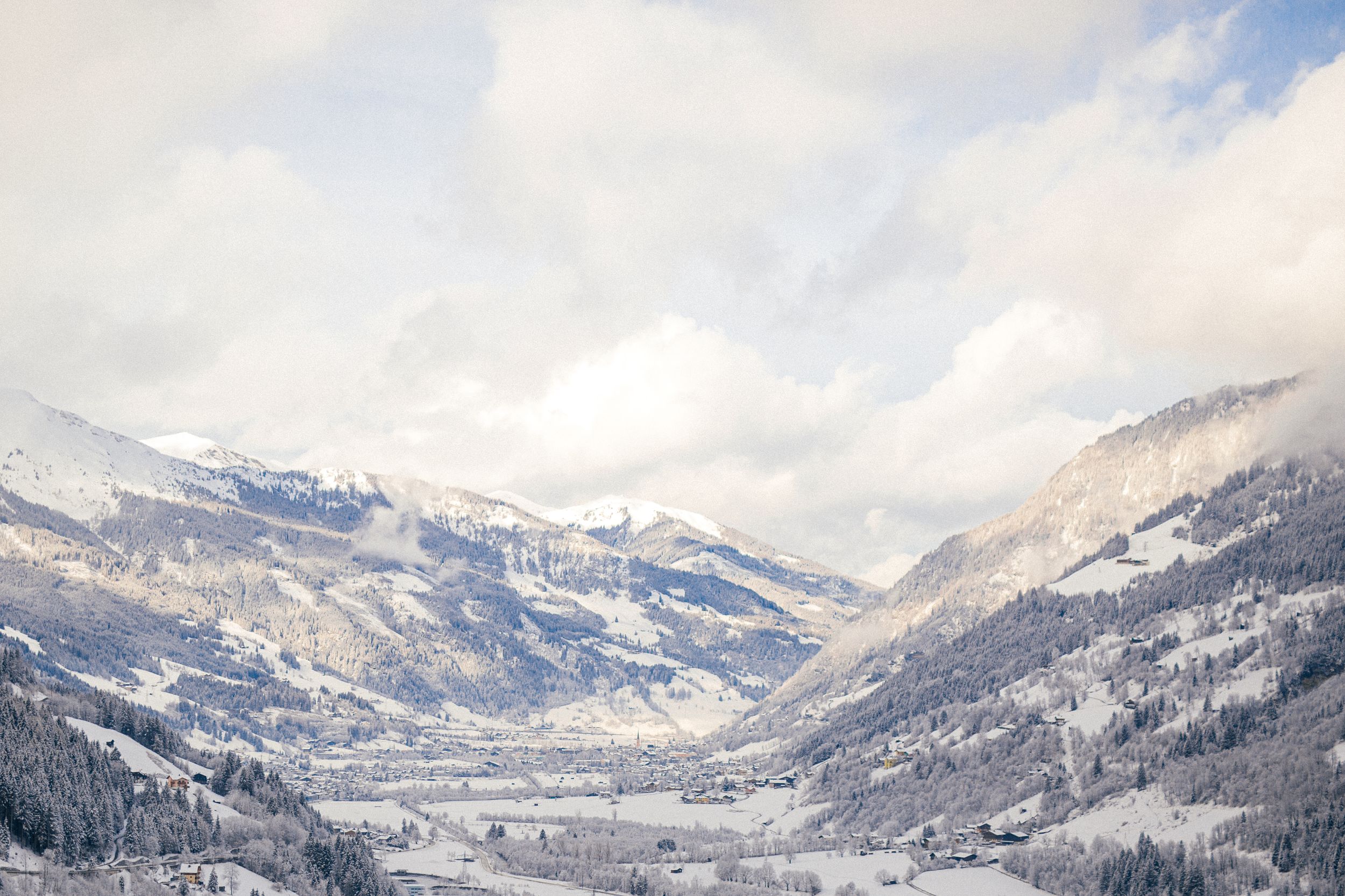 A panoramic winter view of snow-covered mountains and valleys with low-hanging clouds in the Alps.