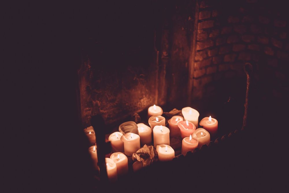 Glowing candles illuminate a dark stone wall in a moody, atmospheric setting.