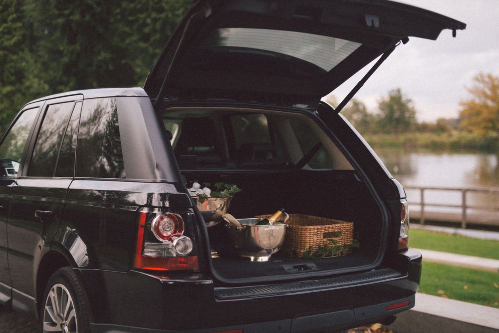 A black SUV with its trunk open parked near a lake during autumn.