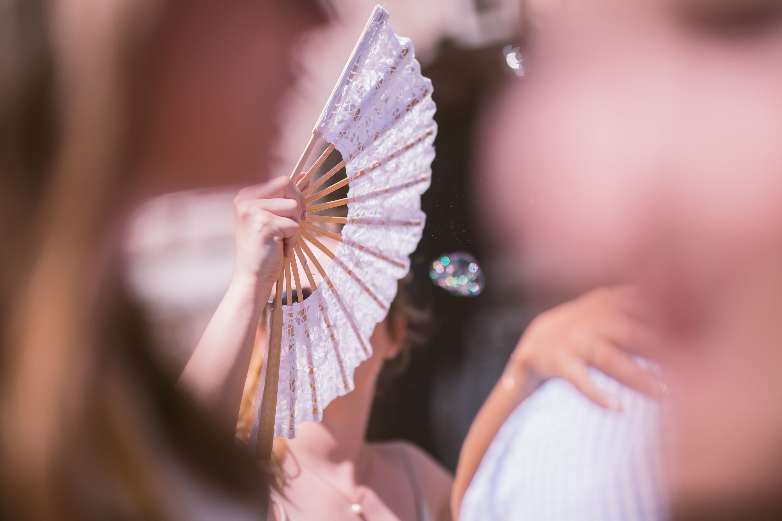 A delicate white paper fan unfolds in a soft pink bokeh background creating an elegant artistic composition.