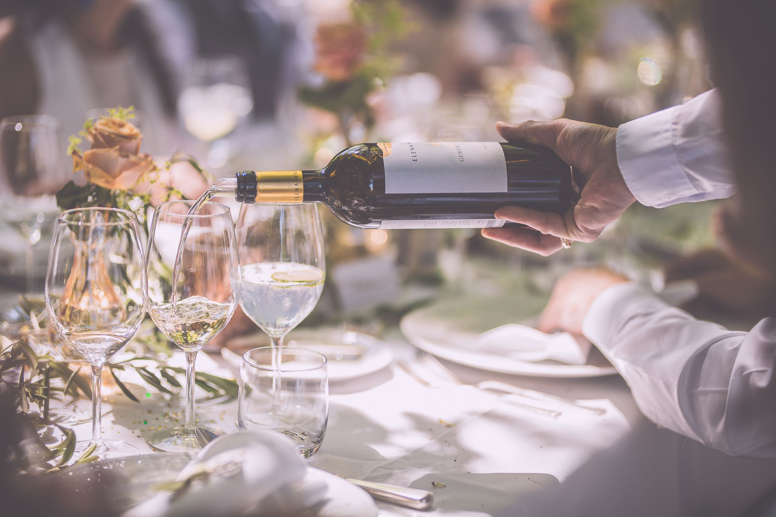 An elegant outdoor dining table setting with glassware and place settings glowing in natural sunlight.