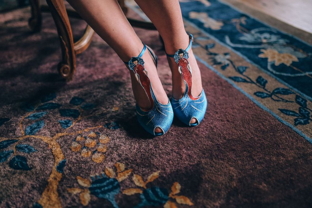 Light blue vintage heels with decorative details shown on feet against a patterned oriental rug background.