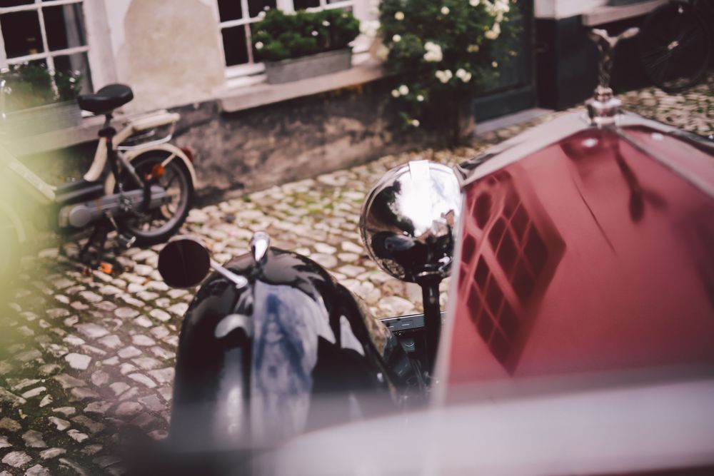 A row of vintage motorcycles parked on cobblestone streets with buildings in the background.