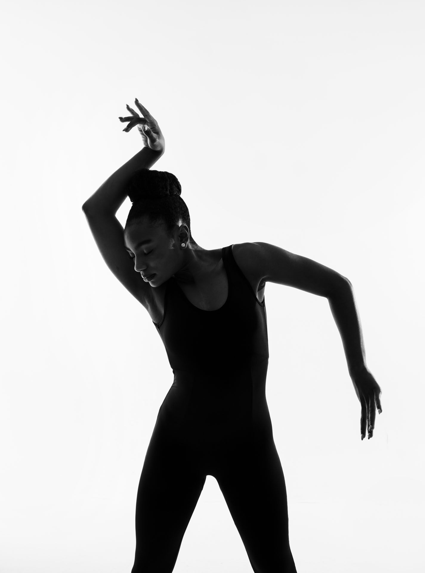 Silhouetted dancers in black outfits perform expressive contemporary dance movements against a white background.