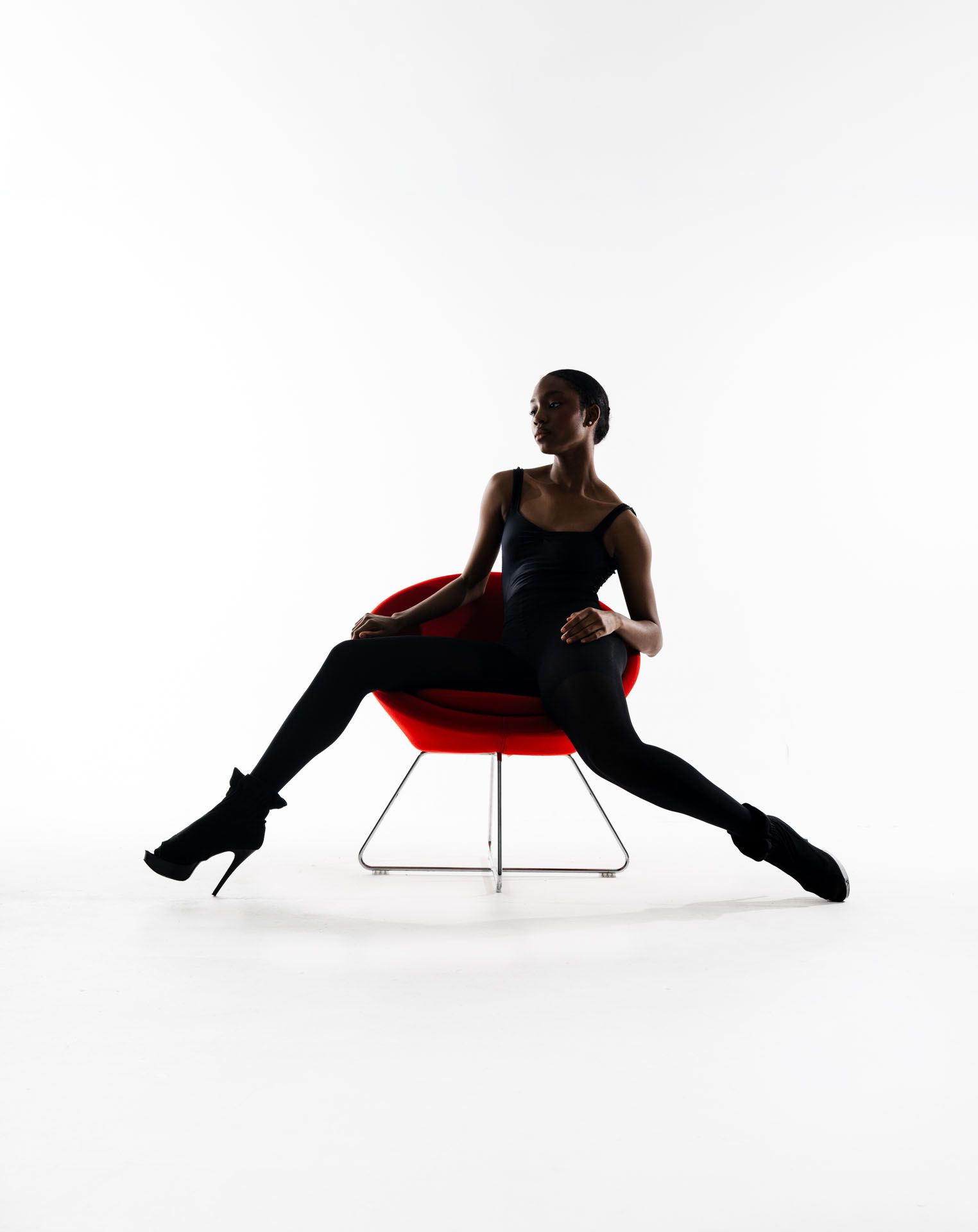 Silhouette of dancer lounging dramatically in a red modern chair against white background.