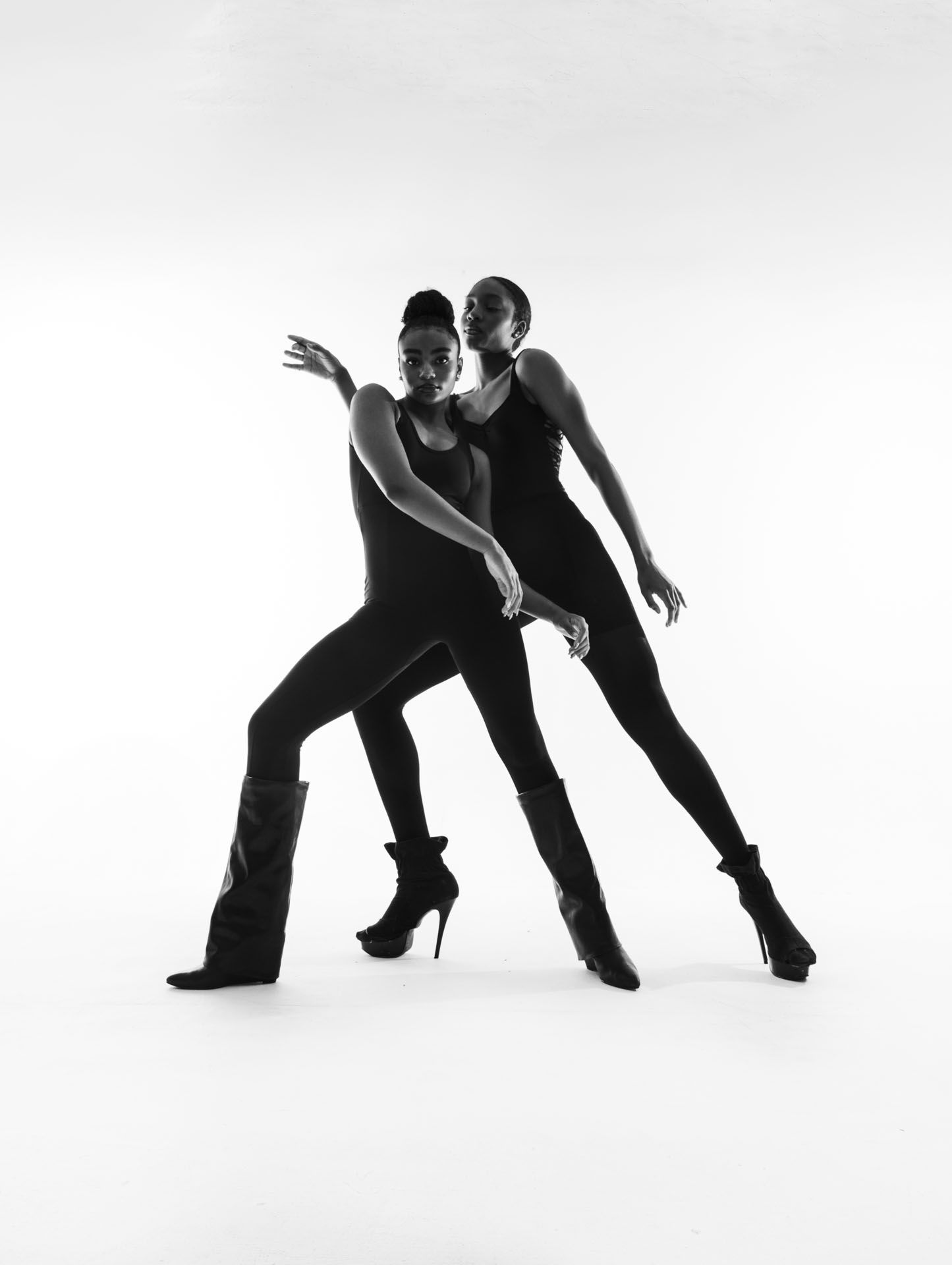 Two dancers in black attire performing contemporary dance moves in artistic silhouette against white background.