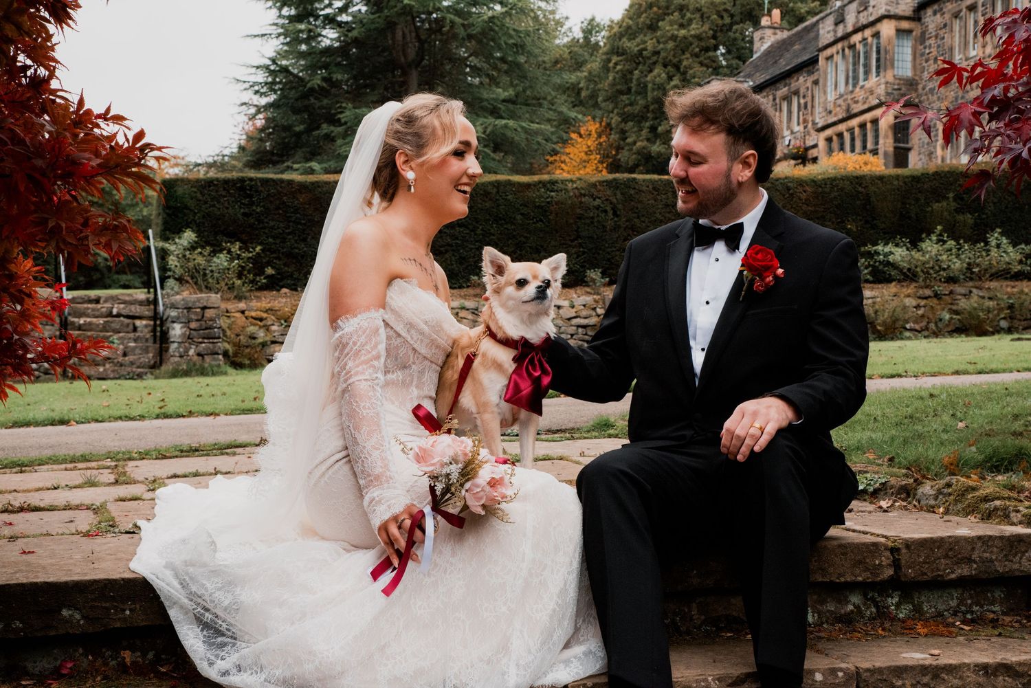 Wedding couple shares romantic moments in an autumn garden with red foliage and their dog.