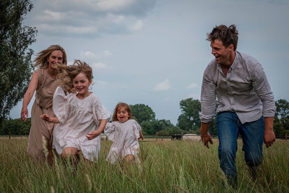 Happy family with two young girls in white dresses running through a lush green meadow together.