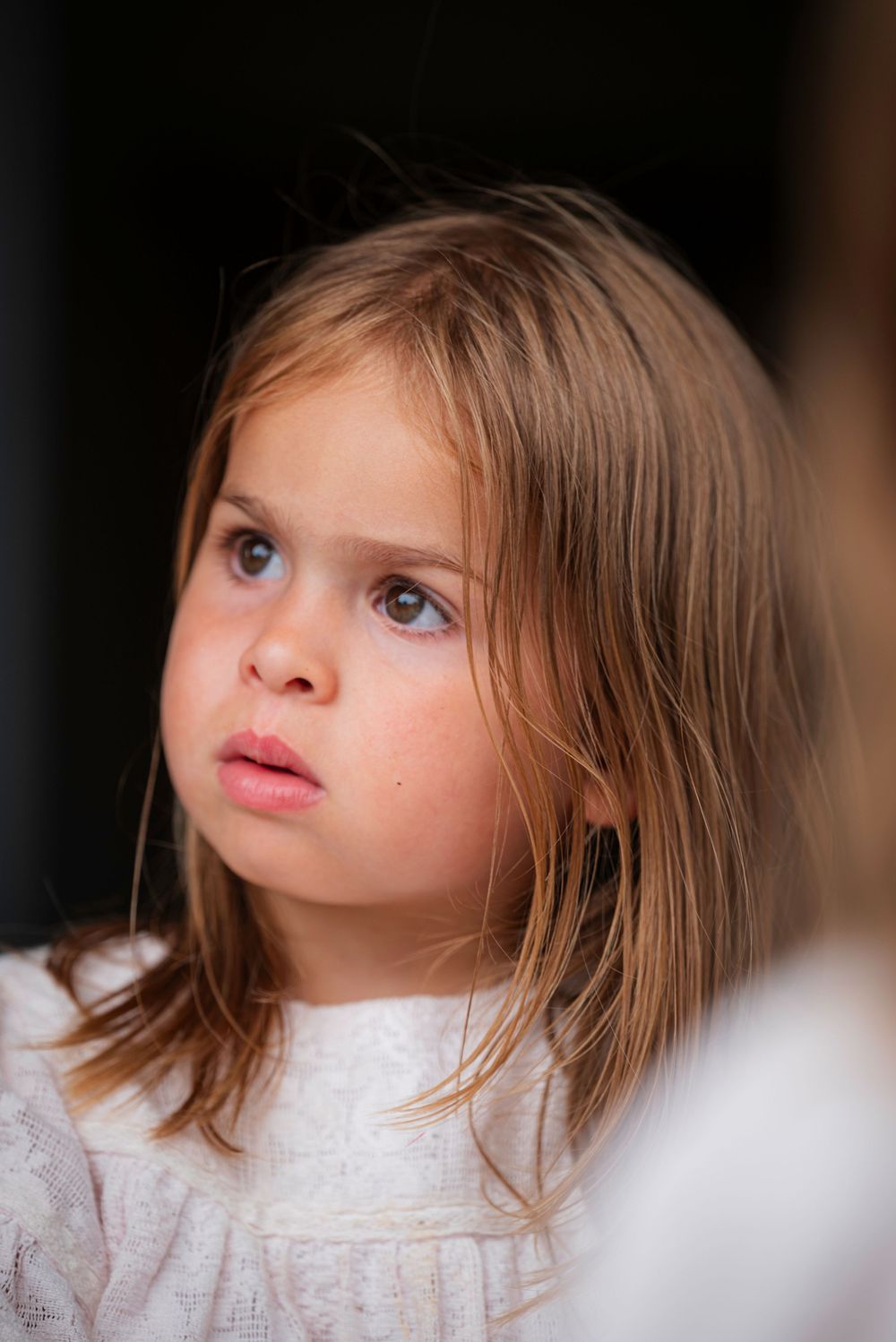 Close-up portrait of a young girl with blue eyes and light brown hair wearing a white dress.
