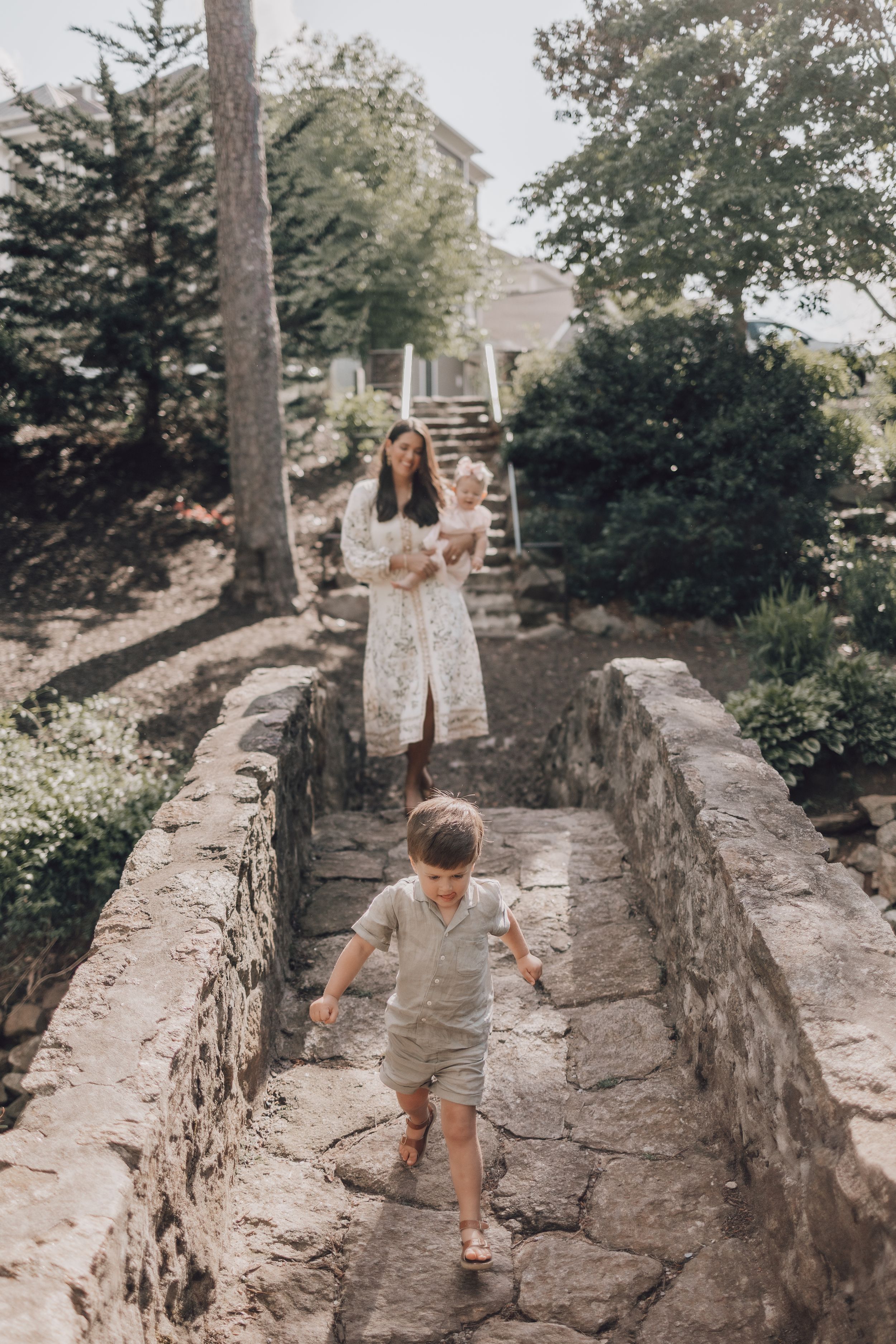 Two people walking along a stone path surrounded by lush garden landscaping on a summer day.
