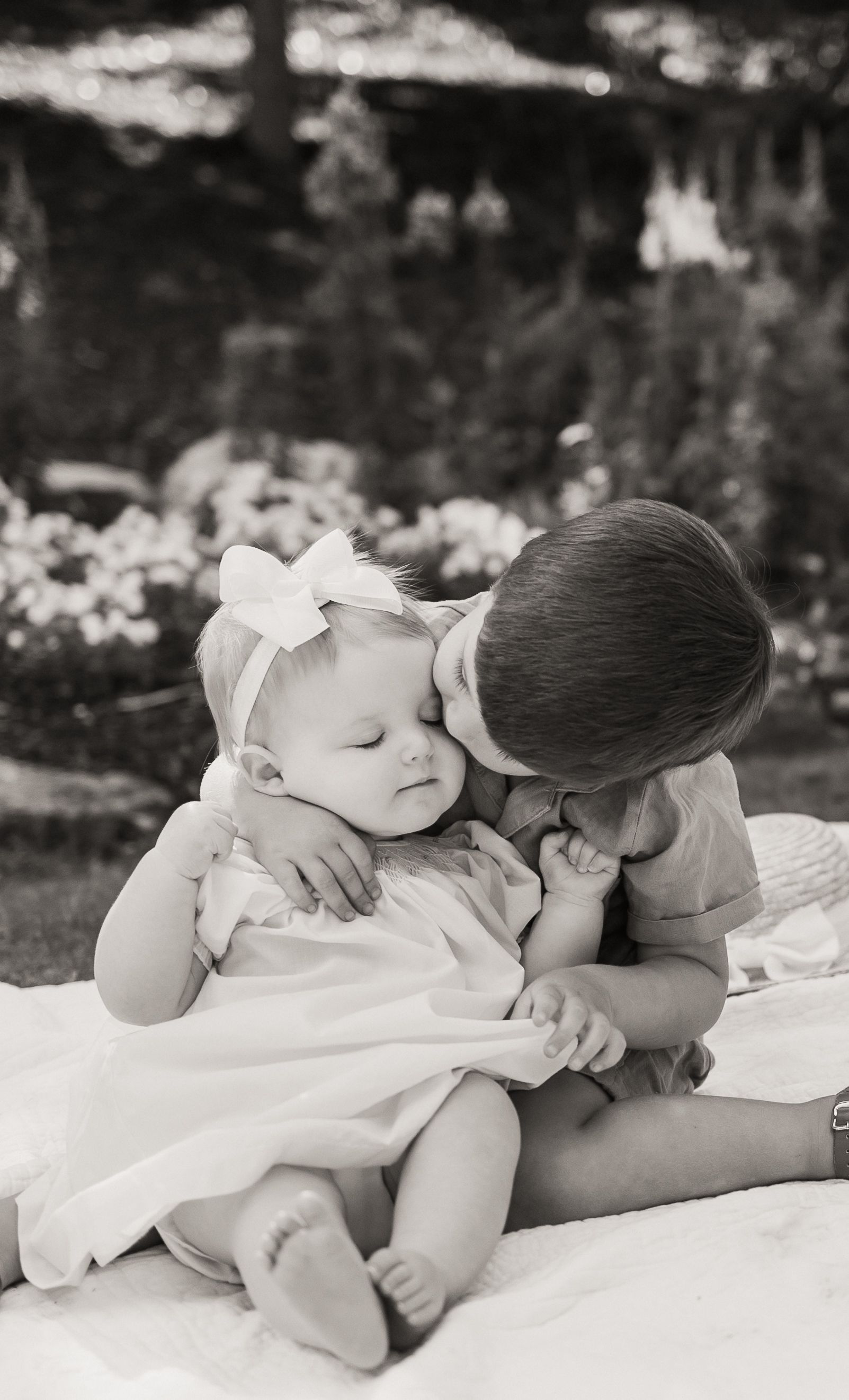 A sweet black and white photo series showing two young children sharing tender moments on a blanket outdoors.