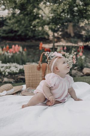 Baby wearing floral crown lies on white blanket outdoors during professional photo session.