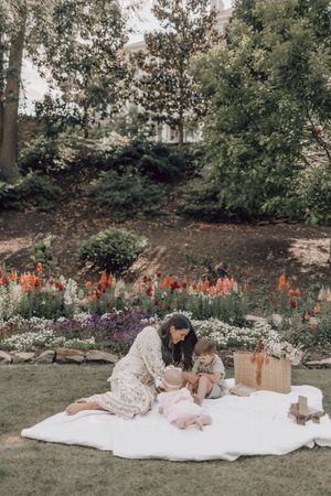 Two children enjoying a summer picnic on a white blanket surrounded by blooming flowers in a garden setting.