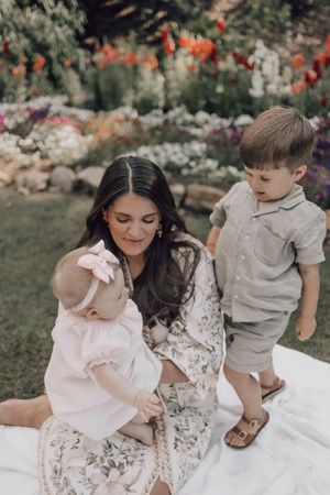 A family sits together on a white blanket in a garden with colorful flowers blooming in the background.