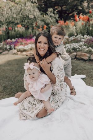 Candid outdoor family moment on white blanket surrounded by blooming garden flowers.