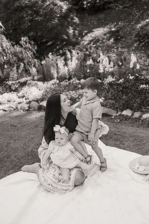 A family enjoying a picnic on a white blanket in a garden with blooming flowers in the background.