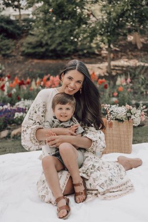 A tender moment shared on a white blanket in a garden setting with flowers in the background.