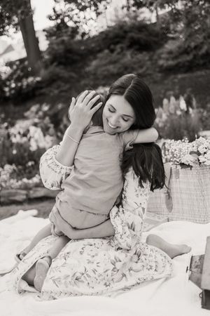 A tender moment captured in black and white of people embracing on a picnic blanket in a garden setting.