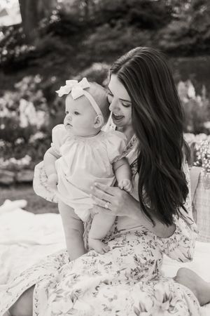 A tender black and white portrait of a parent and baby in matching white outfits sitting outdoors.
