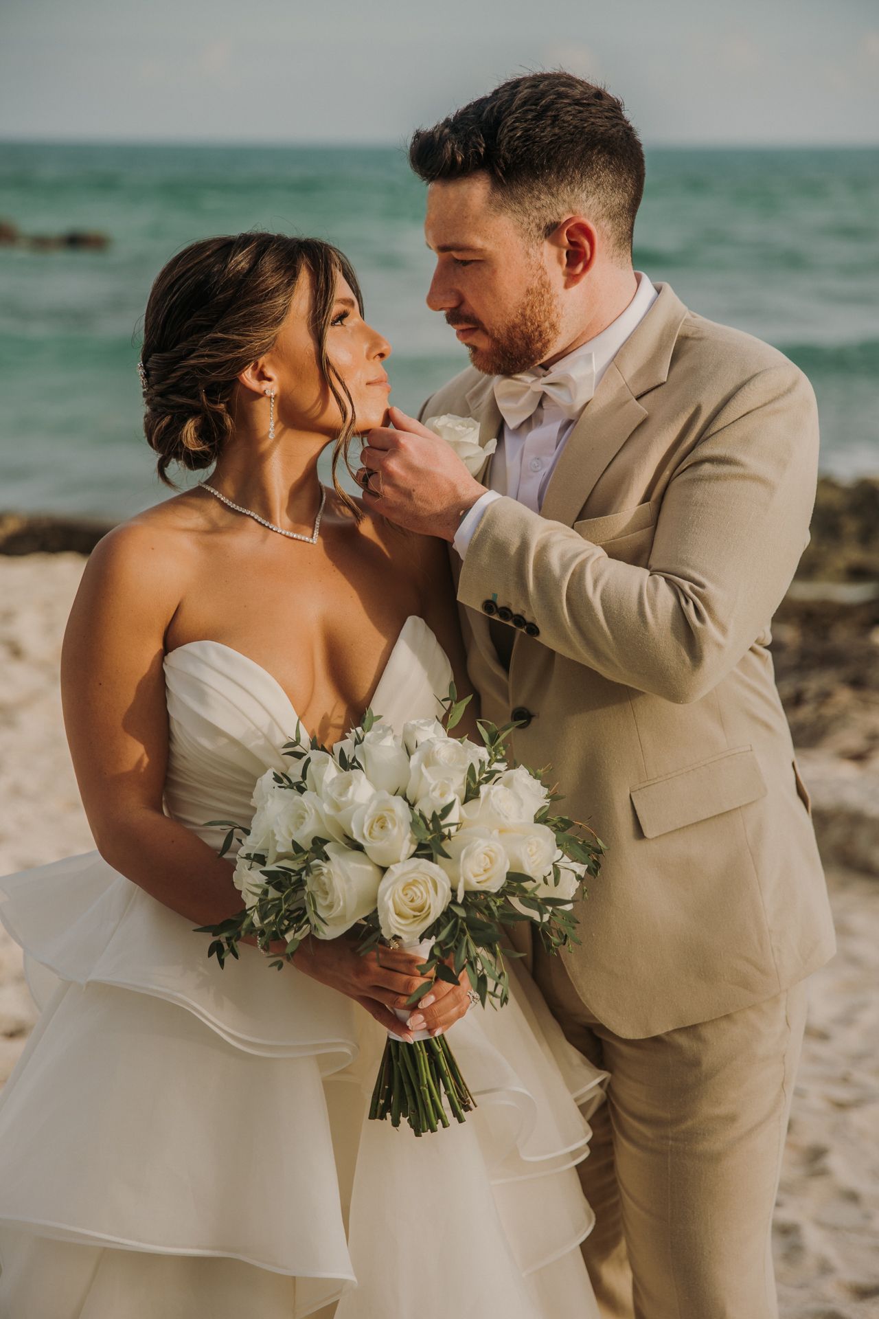 A couple shares intimate moments on a beach during their wedding photoshoot with white rose bouquet. El Dorado Royale Wedding Photographer