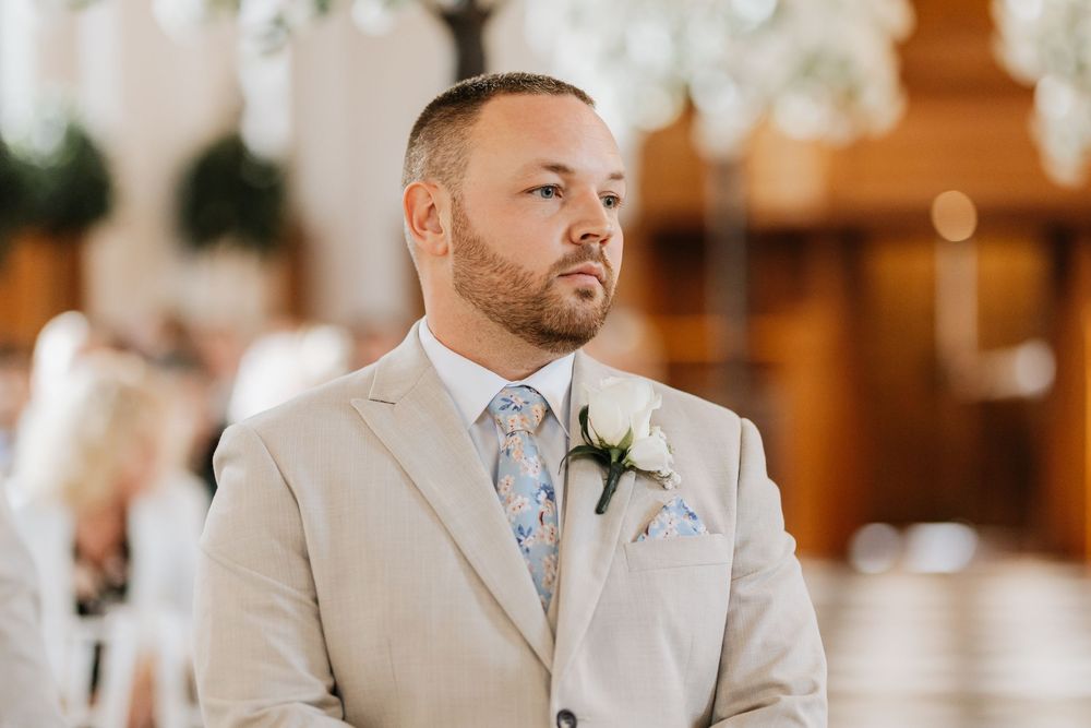 A groom and groomsmen in light beige suits stand together during a wedding ceremony.