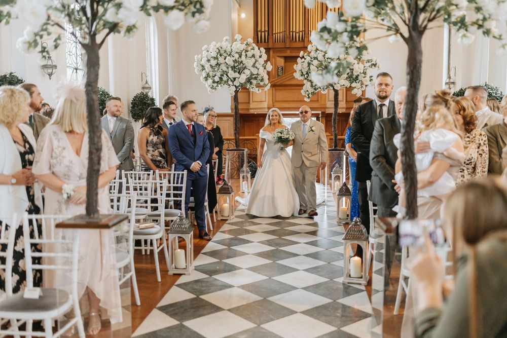 Elegant church wedding ceremony with white floral arrangements and wooden pews along the aisle.