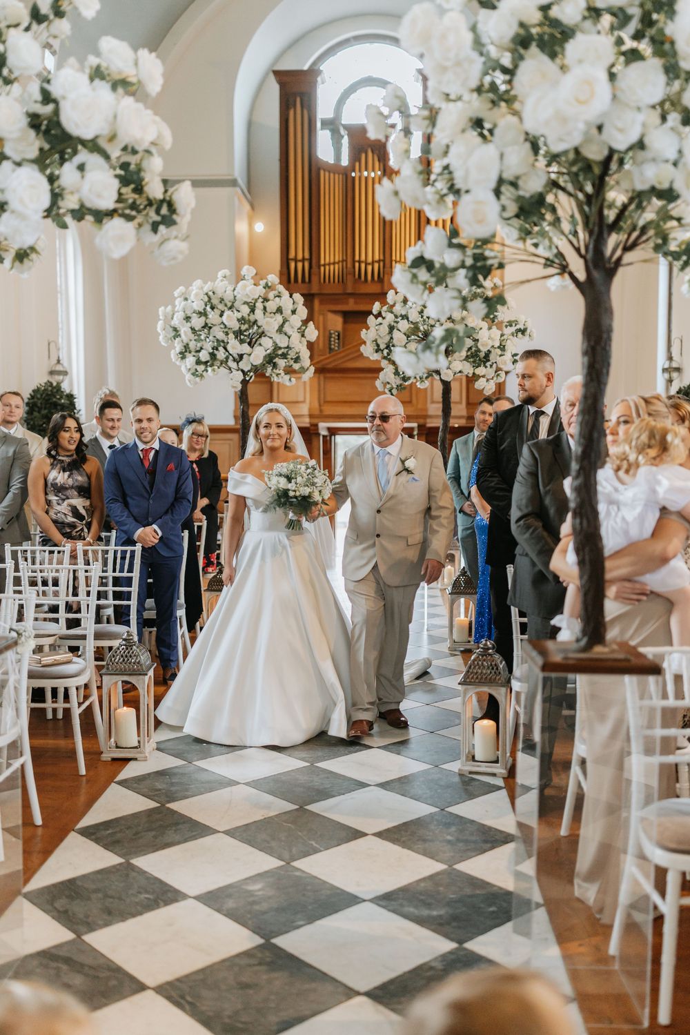 Beautiful church wedding ceremony with white floral decorations, checkerboard floor and wooden pipe organ.