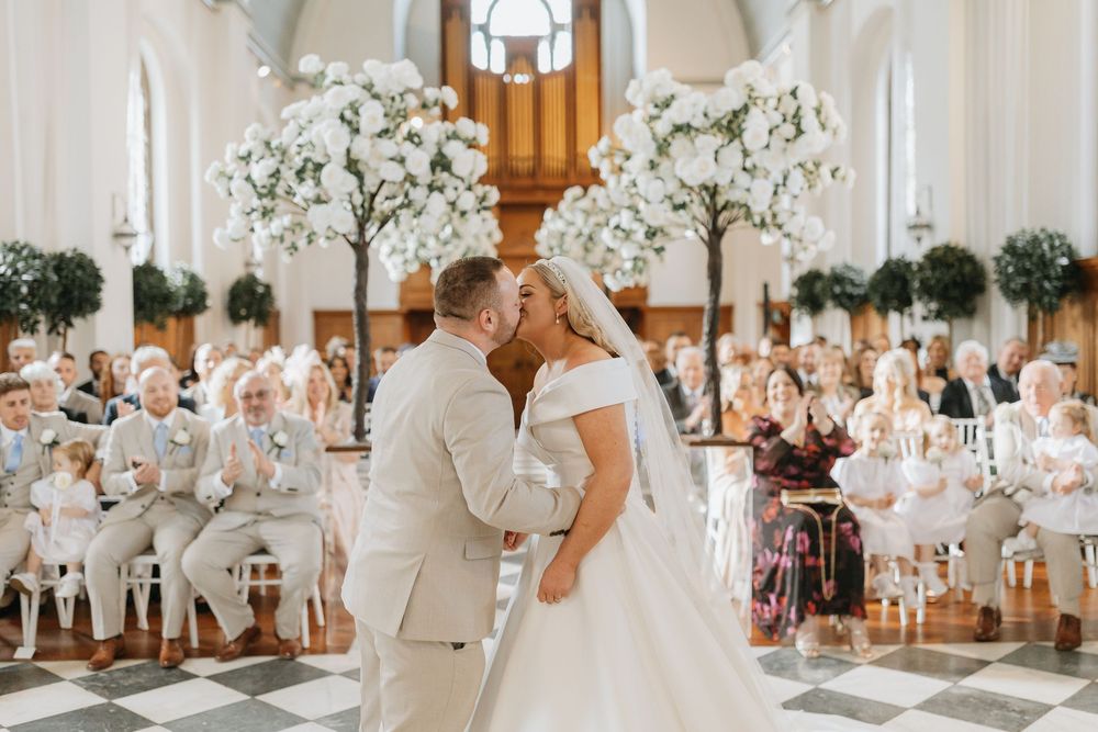 A romantic wedding ceremony in an elegant white church with floral arrangements and candlelit decor.