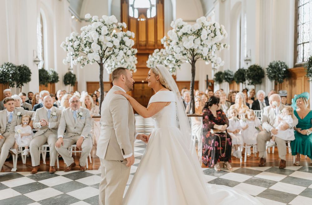 A beautiful wedding ceremony in a white-decorated church with floral arrangements and guests in attendance.
