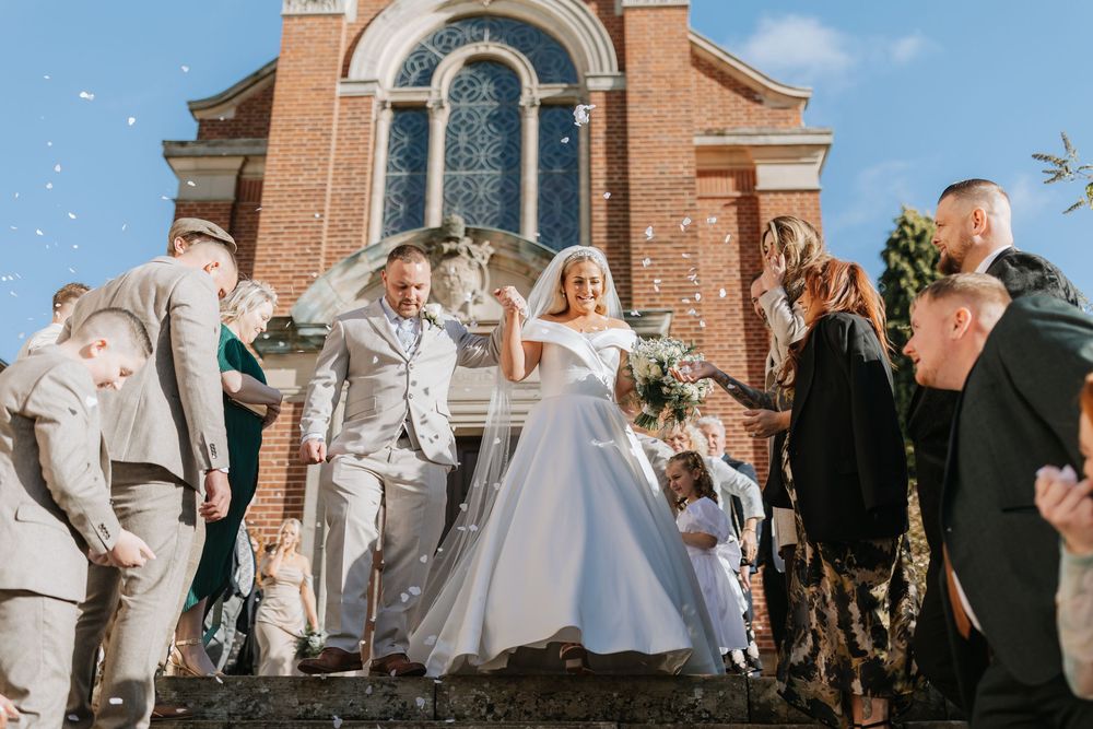 Wedding party poses together outside brick church with arched windows and architectural details.