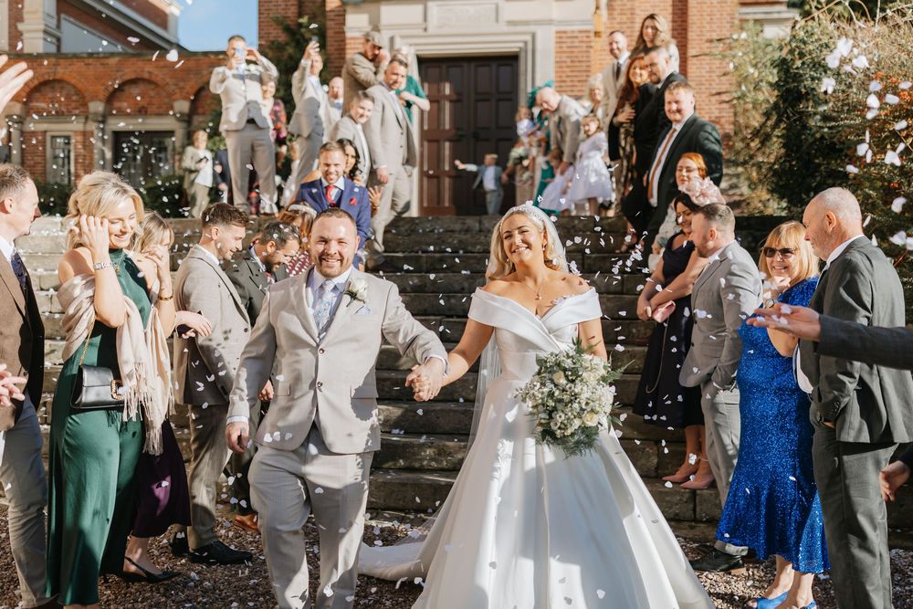 Wedding party celebrates with bubbles and confetti during outdoor ceremony at elegant stone venue.
