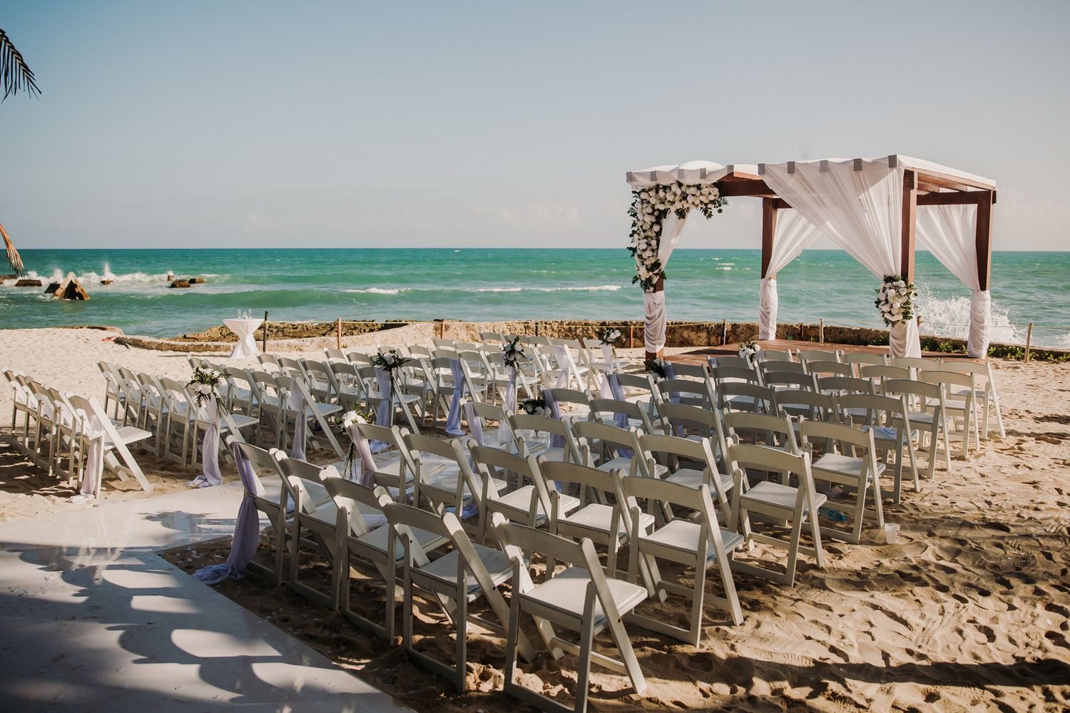 White chairs arranged in rows for an outdoor beach wedding ceremony with ocean views and a wooden arch. El Dorado Royale Wedding Photo