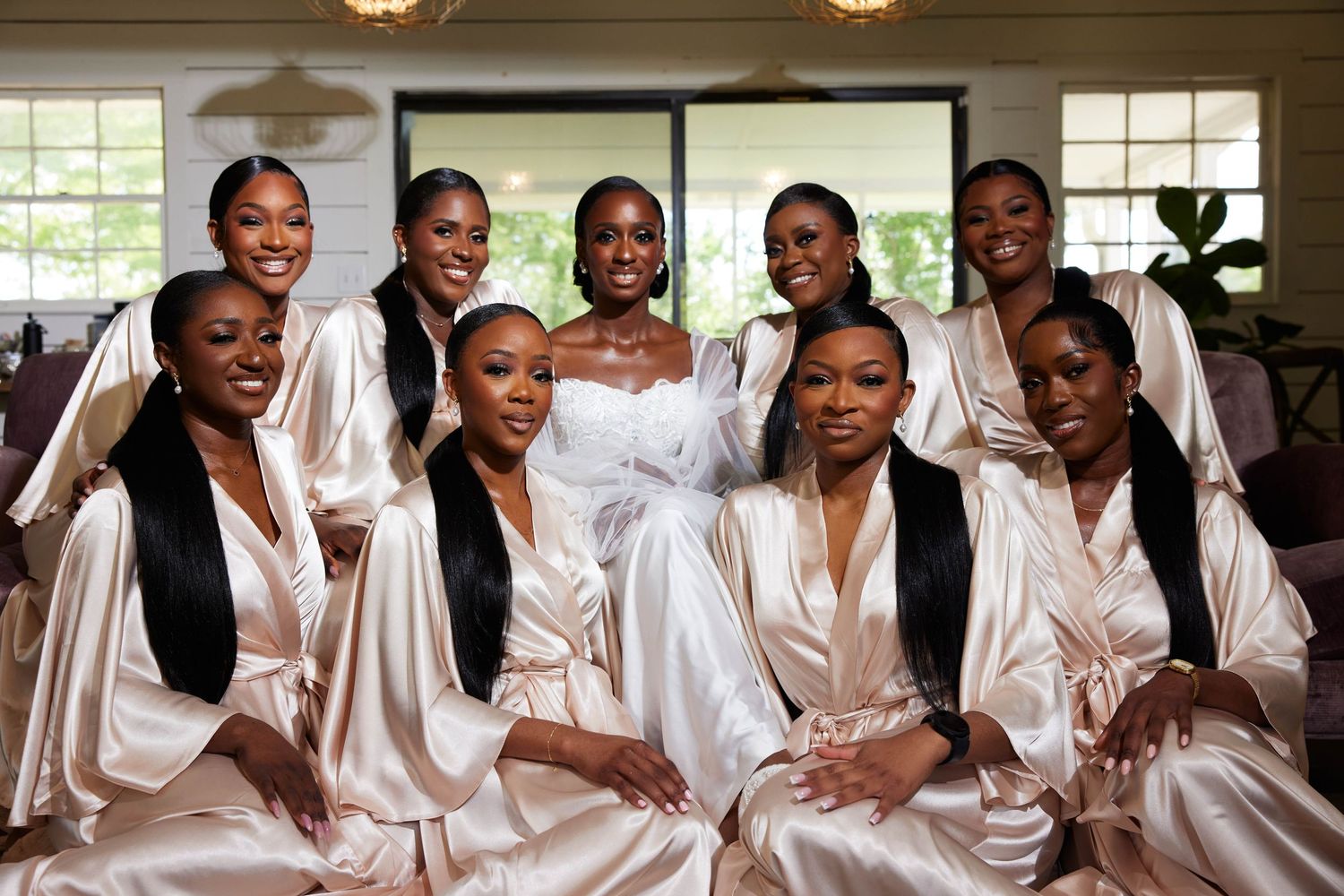 Bride in white gown poses with bridesmaids in champagne satin robes for a elegant bridal party photo.