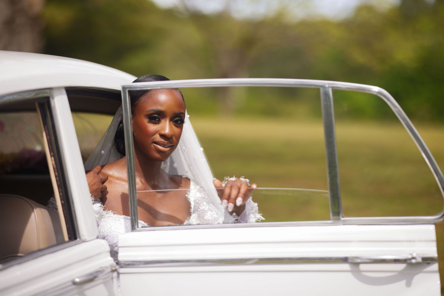 Bride in white wedding dress and veil leaning out of vintage white car window on her wedding day.