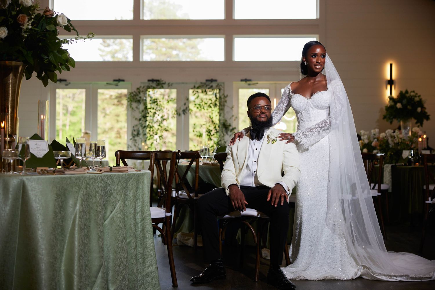Elegant Black couple in wedding attire pose at reception, bride in white gown with veil, groom in white suit.