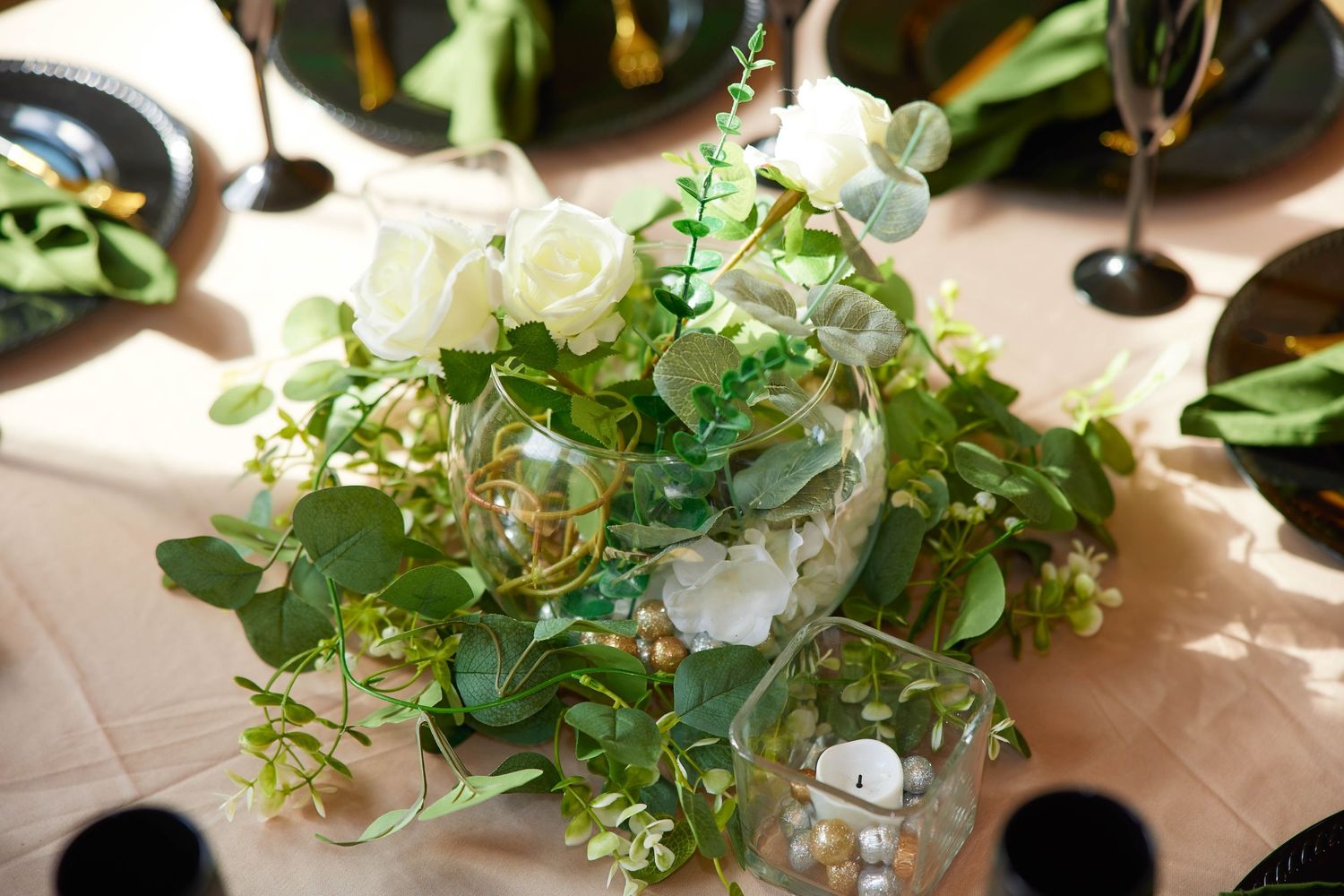 Elegant floral centerpiece with white roses and lush greenery in a glass bowl on a table.