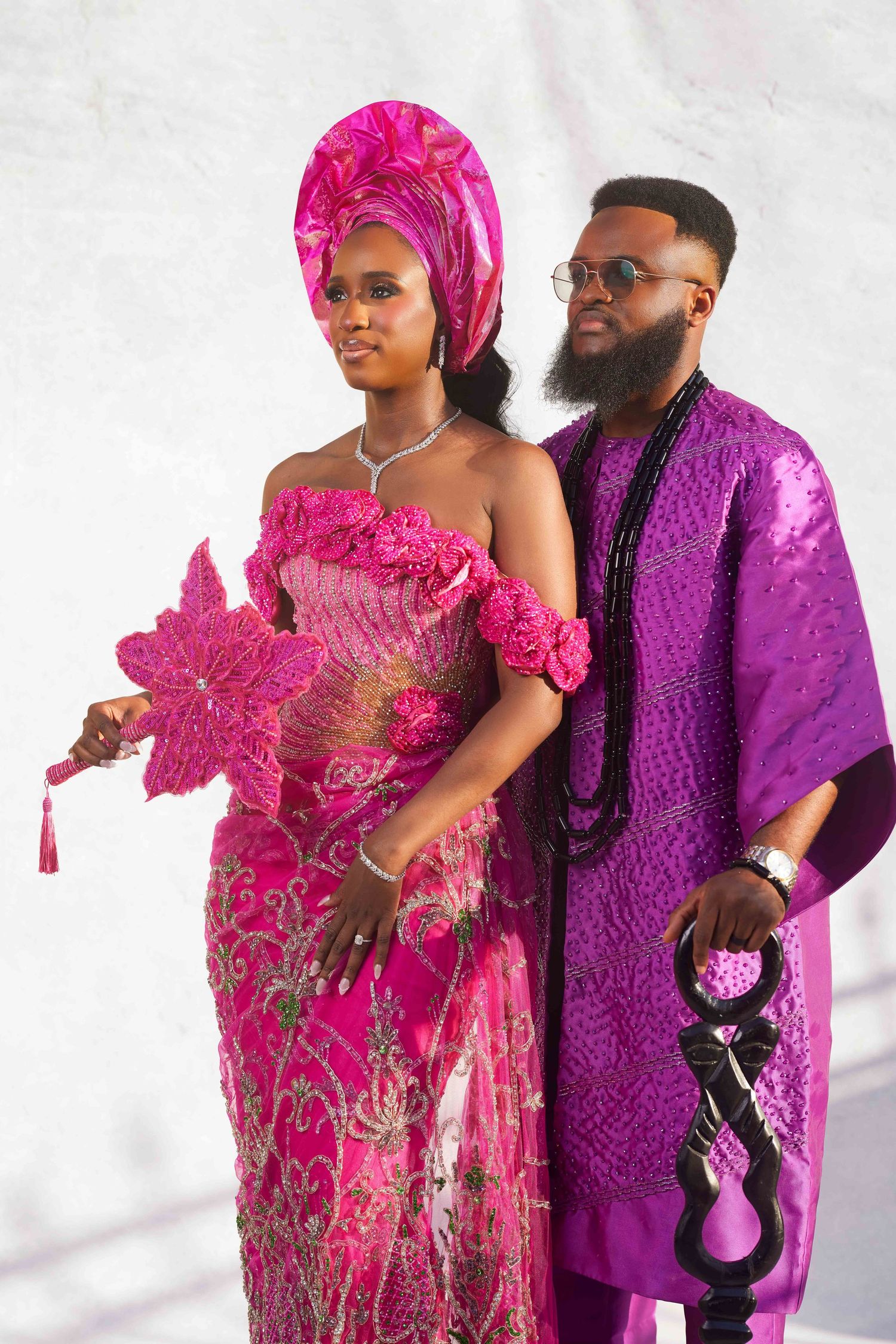 Nigerian couple in traditional pink and purple attire posing elegantly for a cultural wedding ceremony.
