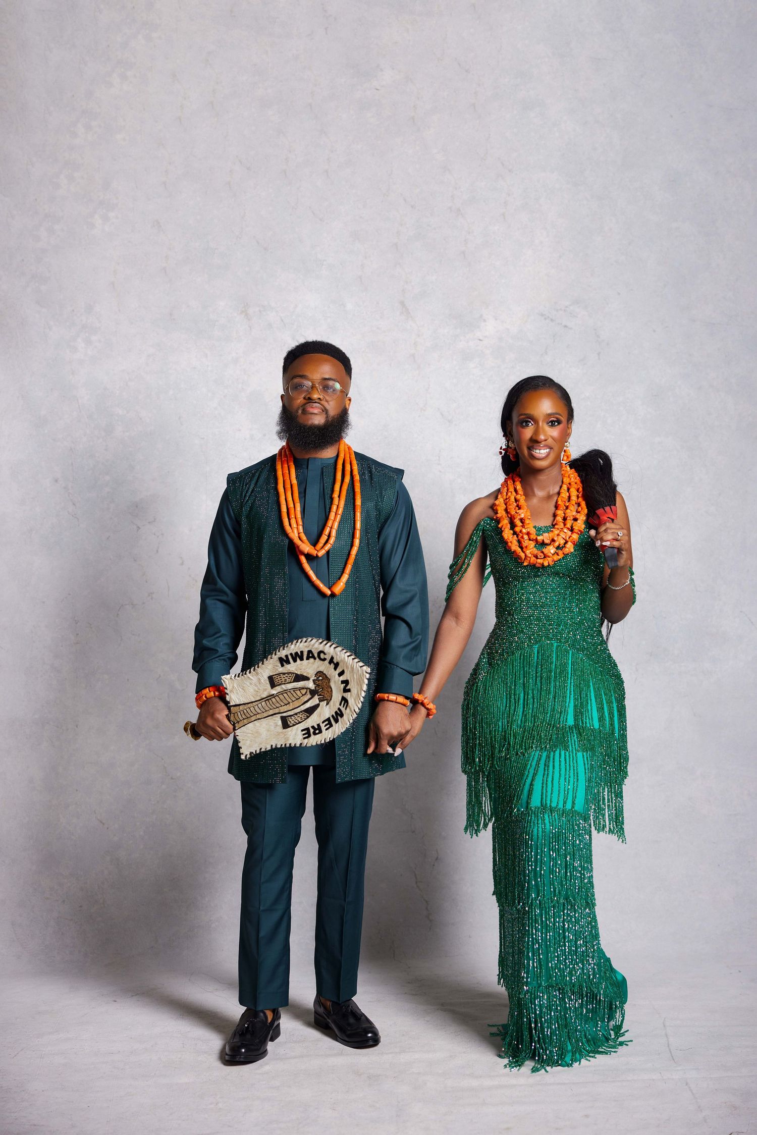 Nigerian couple in traditional green attire with orange coral beads posing for a portrait photo.